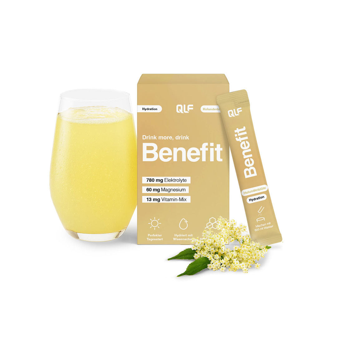Yellow hydration drink in glass with beige Quantum Leap Fitness Benefit sachet, box, and white elderflowers on white background