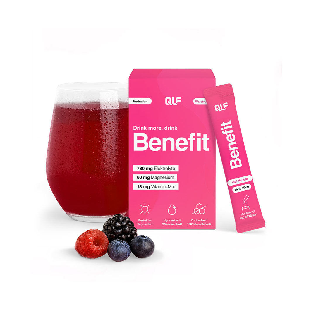 Glass of dark red beverage with blackberry, raspberry, and blueberries alongside bright pink Benefit by QLF sachet and box on white background
