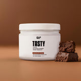 Tasty Kalorienarmes Geschmackspulver Chocolate Fudge mit Kakaostückchen und zwei Schokostücken vor braunem Hintergrund