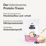 Auf der Verpackung eines proteinreichen Puddings mit der Aufschrift "Eiweiß" befindet sich ein Löffel Pudding mit Heidelbeeren. Der deutsche Text wirbt für Eiweiß zum Muskelaufbau, zur Unterstützung von Diäten und für eine lang anhaltende Sättigung.
