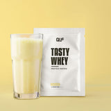 Tasty Whey Proteinpulver Eierlikör Sachet mit cremigem Shake im Glas vor gelbem Hintergrund Galerie 1