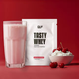 Tasty Whey Proteinpulver Kirsche Joghurt mit Shake im Glas, Sahne und frischen Kirschen vor rotem Hintergrund Galerie 1