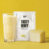 Tasty Whey Proteinpulver Lemoncake mit Shake im Glas und Stück Zitronenkuchen vor gelbem Hintergrund Galerie 1
