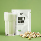 Tasty Whey Proteinpulver Pistazie mit cremigem Shake, Pistazien und Sachet vor grünem Hintergrund Galerie 1