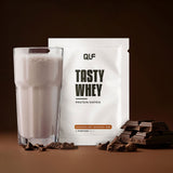Tasty Whey Proteinpulver Schokolade weniger süß mit Shake im Glas und Schokostücken vor dunklem Hintergrund Galerie 1
