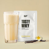Tasty Whey Proteinpulver Vanille weniger süß mit Shake im Glas, Vanilleschote und Blüte vor beigem Hintergrund Galerie 1