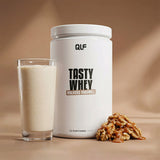 Tasty Whey Proteinpulver Walnuss Karamell mit cremigem Shake im Glas und Walnüssen vor beigem Hintergrund Galerie 1