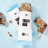 Tasty Bar Proteinriegel Milky Kokos mit 17g Protein, teilweise ausgepackt auf hellblauem Hintergrund, Galerieposition 1