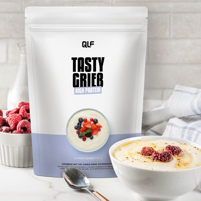 White and light blue bag of Quantum Leap Fitness Tasty Grieb high protein with bowl of creamy porridge topped with berries nearby