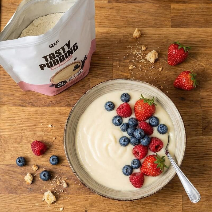 A bowl of creamy pudding topped with fresh strawberries, raspberries, blueberries, next to a bag of QLF Tasty Pudding powder.