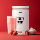 Tasty Whey Proteinpulver Erdbeer Sahne mit Shake im Glas, frischen Erdbeeren und cremigem Topping vor rotem Hintergrund
