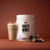 Tasty Whey Proteinpulver Mozartkugel mit cremigem Shake im Glas und Mozartkugeln vor braunem Hintergrund