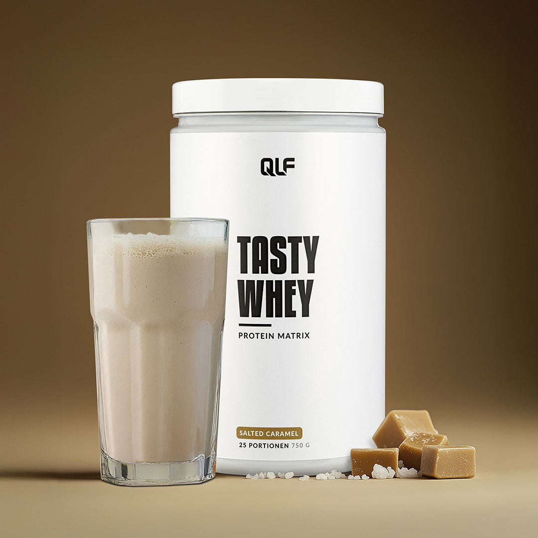 Tasty Whey Proteinpulver Salted Caramel mit Shake im Glas und Karamellstücken vor braunem Hintergrund Galerie 1