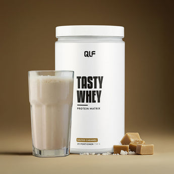 Tasty Whey Proteinpulver Salted Caramel mit Shake im Glas und Karamellstücken vor braunem Hintergrund Galerie 1