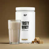 Tasty Whey Proteinpulver Salted Caramel mit Shake im Glas und Karamellstücken vor braunem Hintergrund Galerie 1