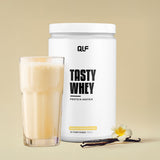 Tasty Whey Vanille weniger süß Proteinpulver mit Shake im Glas und Vanilleschote vor beigem Hintergrund Galerie 1