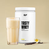 Tasty Whey Vanille Proteinpulver mit Glas Shake, Vanilleschote und Blüte auf beige Hintergrund, Galerieposition 1